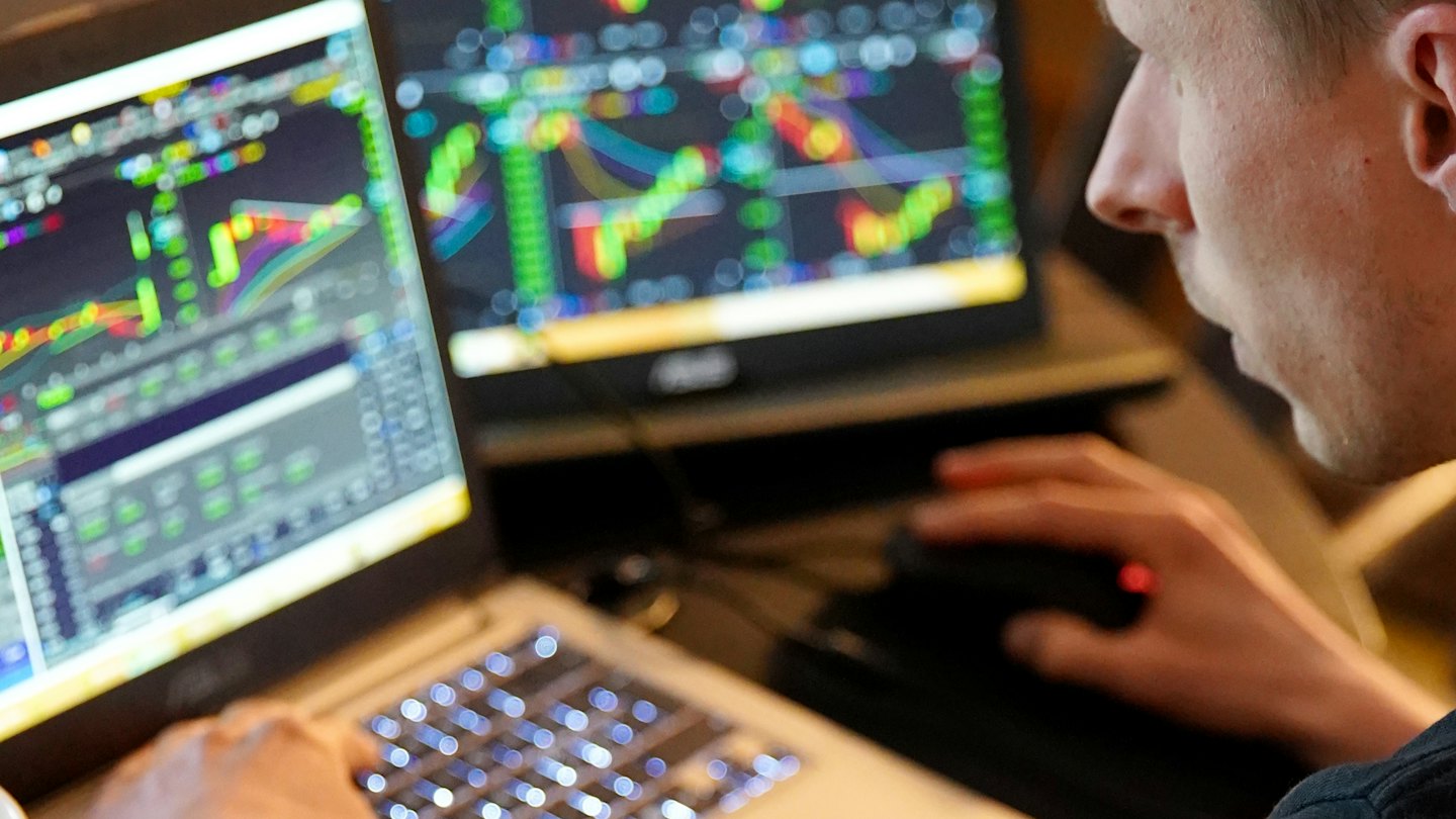 Uomo che analizza grafici finanziari su più schermi con un laptop.